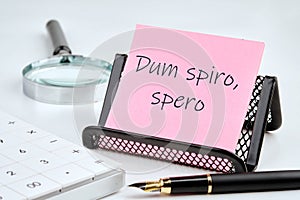 Dum Spiro Spero - latin phrase means While I Breath, I Hope. on a pink sticker with office supplies on a white background photo