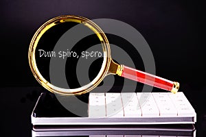 Dum Spiro Spero - latin phrase means While I Breath, I Hope. through a magnifying glass on a black background in white font photo