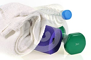 Dumbbell next to a water bottle, towel and rolled up gym mat