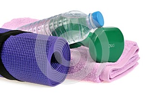 Dumbbell on a towel next to a water bottle and a rolled up gym mat