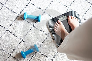 Dumbbell and woman`s leg on weight scale, symbolic of diet and weight loss