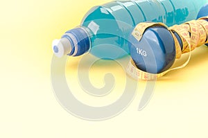 Dumbbell with yellow centimeter and bottle/blue dumbbell with centimeter and bottle on a yellow background. Copy space