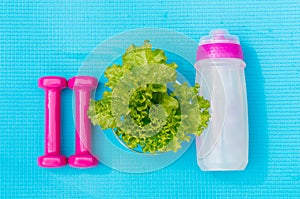 Dumbbells, bottle of water and salad leaves on yoga mat