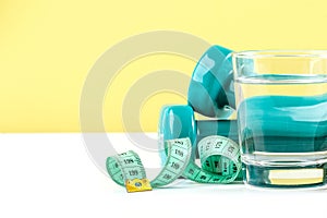 Dumbbells, centimeter and a glass of water on a white-green background