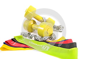 Dumbbells, colored fitness rubber bands and a measuring tape on white