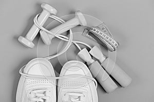 Dumbbells in cyan blue color on white trainers, top view. Sneakers with skipping rope and tape on green background.