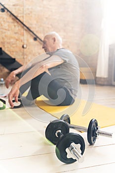 Dumbbells and elderly man relaxing after his fitness workout at home