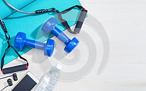 dumbbells, excercise equipment, gym yoga mat, cellphone, earphones, and bottle of water on clean wood floor with strong bright mo