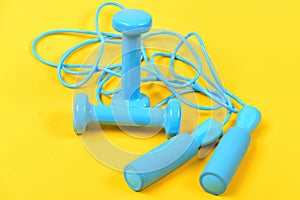 Dumbbells and jump rope in cyan blue color on yellow