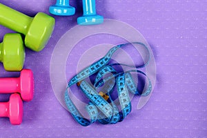 Dumbbells and measure tape in cyan color on purple texture