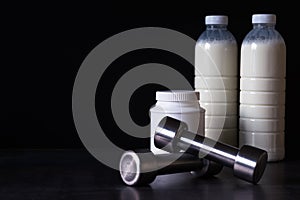 Dumbbells with protein powder and milkshake bottles in plastic packaging on a dark metal background. Background.