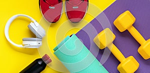 Dumbbells on purple roll mat on yellow background. Sport lifestyle concept. Flat lay. Red sneakers, music headphones, earphones