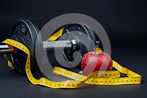 Dumbbells, tape measure and an apple on a dark background