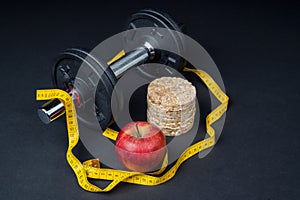 Dumbbells, tape measure and an apple on a dark background