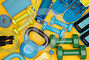 Dumbbells, trainers, jumping rope and other fitness equipment on yellow background