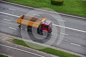 Dump truck carries sand along a road in a city. View from above. Object in motion, soft focus, possible graininess