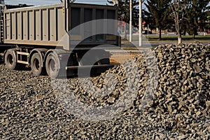 A dump truck is dumping gravel on a construction site. Dump truck dumps its load of gravel on a new road construction