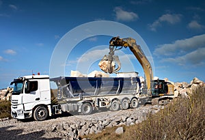 dump truck unloading its cargo on a construction site with the help of an excavator equipped with a grapple
