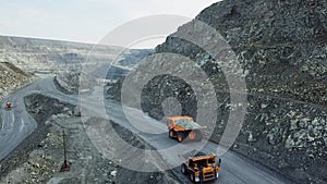 Dump truck is at quarry. Top view of driving orange dump truck with rubble on road open pit. Heavy transport in mining