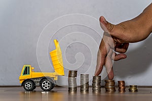 Dump truck toy downloading a coins stack, hand as finger running on heap of coins