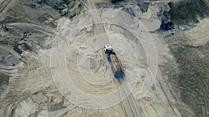 Dump truck transported sand from the open pit. Truck with tipper semi trailer working in quarry. Arial view of the opencast mine.