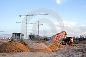 Dump truck unloading earth sand for road construction or for foundation work. Work of tower crane at construction site on blue sky