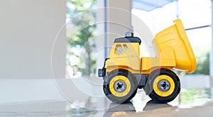 Dump truck, yellow construction toy vehicle with articulated parts built with sturdy plastic is placed on a table