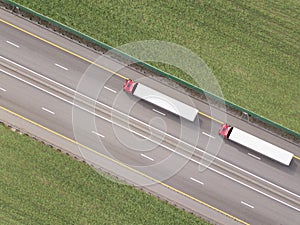 Dump trucks carrying goods on the highway. Red truck driving on asphalt road along the green fields. seen from the air