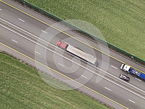 Dump trucks carrying goods on the highway. Red truck driving on asphalt road along the green fields. seen from the air