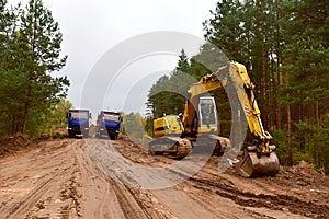 Dump trucks and excavator work on road construction in a forest zone. Tipper truck transport sand for roadworks project