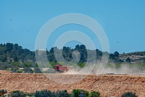 A dumper truck drives along the dusty road in the hot midday sun