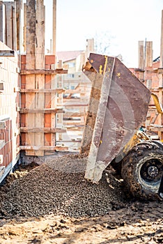 Dumper truck unloading construction gravel, granite and crushed stones at building foundation