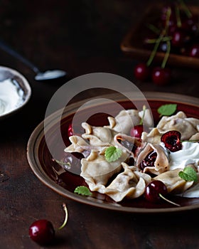 Dumplings with cherries and sour cream sauce on a plate, one cut, visible toppings.