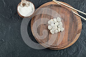 Dumplings plate and bowl of flour on dark surface