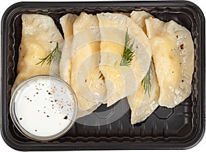 Dumplings with sour cream in a disposable rectangular plastic black lunch box top view on a white background