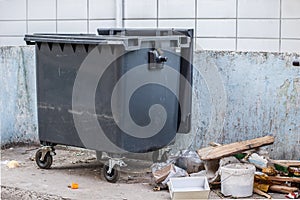 Dumpster on the grey wall background. Garbage bin near housing