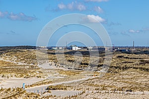Dune landscape with hills, marram grass, hiking trails and the reactor center in the background