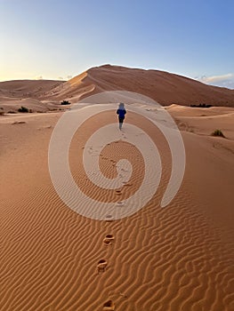 Dunes in the Sahara desert, Merzouga, panoramic view. Morocco. Sunset. A girl walking on the sand dune