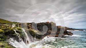 Dunseverick Falls with small cliffs and streaks of water falling down to Atlantic Ocean, Northern Ireland