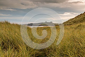 Dunstanburgh Castle in Northumberland, England, through the dune grass with cloudy skies overhead