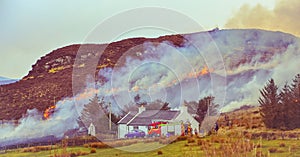 Dunvegan/Scotland, March 2014: Fire brigade trying to control a dry grass and reeds fire near residential buildings