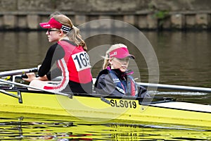 Two young female athele rowers in a yellow boat waiting for a regatta race to start looking bored and cold