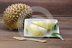 Durian fruits and yellow flesh durian on white dish with durian leaf, wooden background.