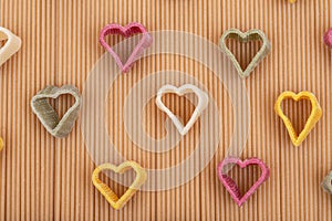 Durum wheat semolina heart-shaped 5 flavors pasta with vegetables arranged on a brown rice spaghetti pasta background.