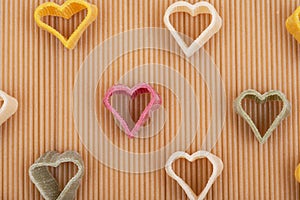 Durum wheat semolina heart-shaped 5 flavors pasta with vegetables arranged on a brown rice spaghetti pasta background.