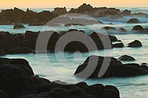 Dusk background of sunset and blurred waves crashing on rocky coastline near Monterey, California, USA