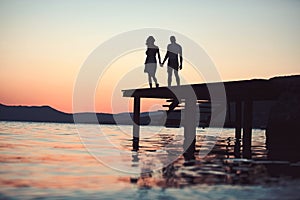 Dusk couple silhouette on pier at sea water. dusk couple silhouette walk at sunset sea resort.