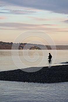 dusk or dawn man silhouetted fishing in water