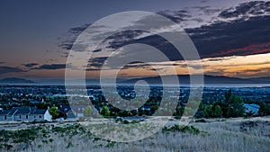 Dusk falls over a sleepy city in a valley with mountains and a lake in the background