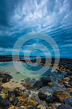 Dusk over ocean volcanic rock pool on a cloudy sky